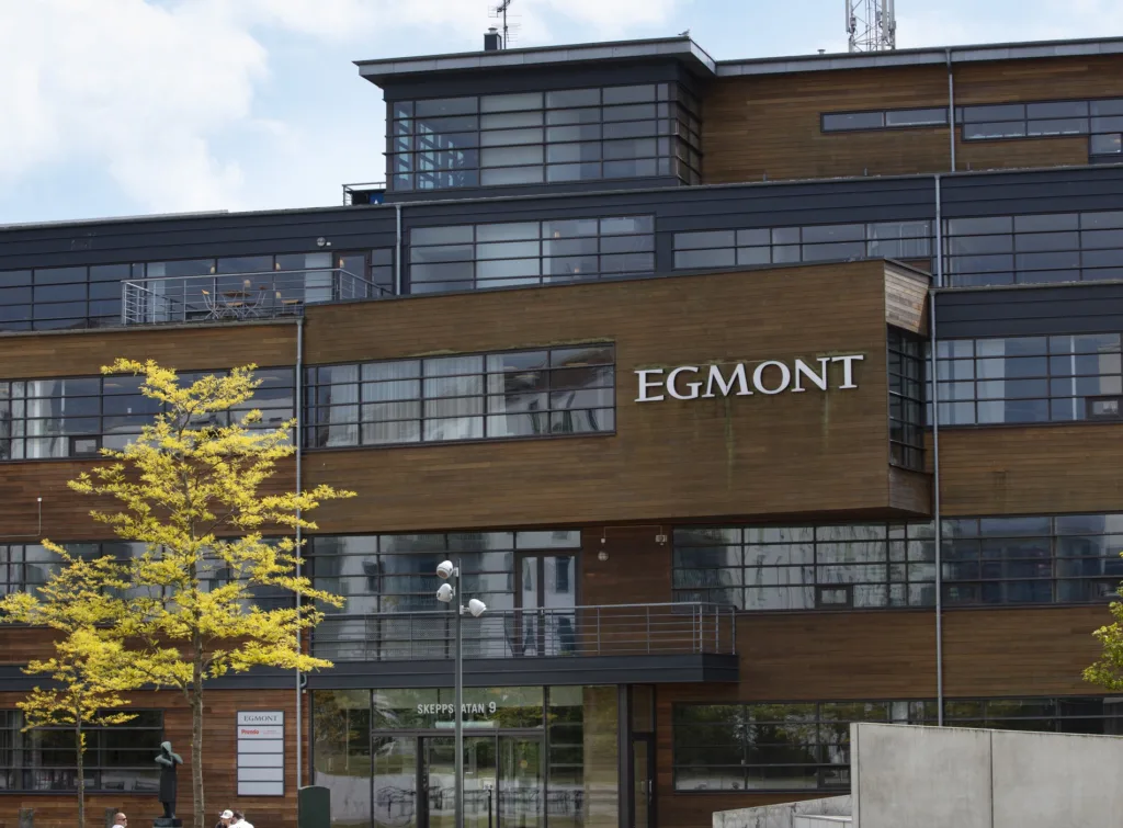 4. En modern byggnad med skylten "EGMONT" på fasaden, omgiven av träd och glaspartier.