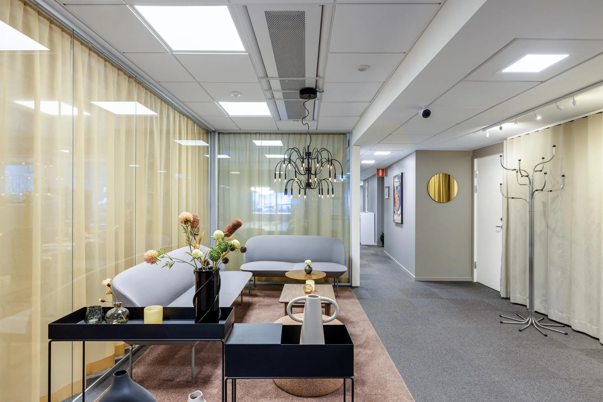 Ett modernt väntrum med soffa, soffbord, blommor och ljus inredning.