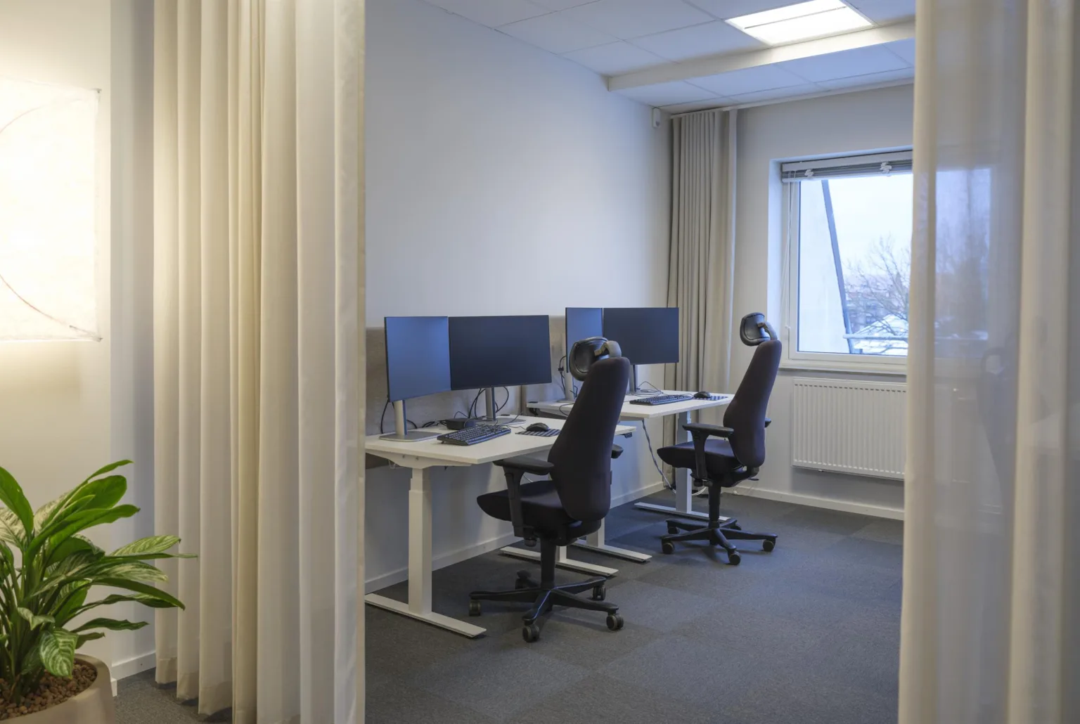 2. Ett kontorsrum med två skrivbord, skärmar och svarta kontorsstolar bredvid ett fönster.