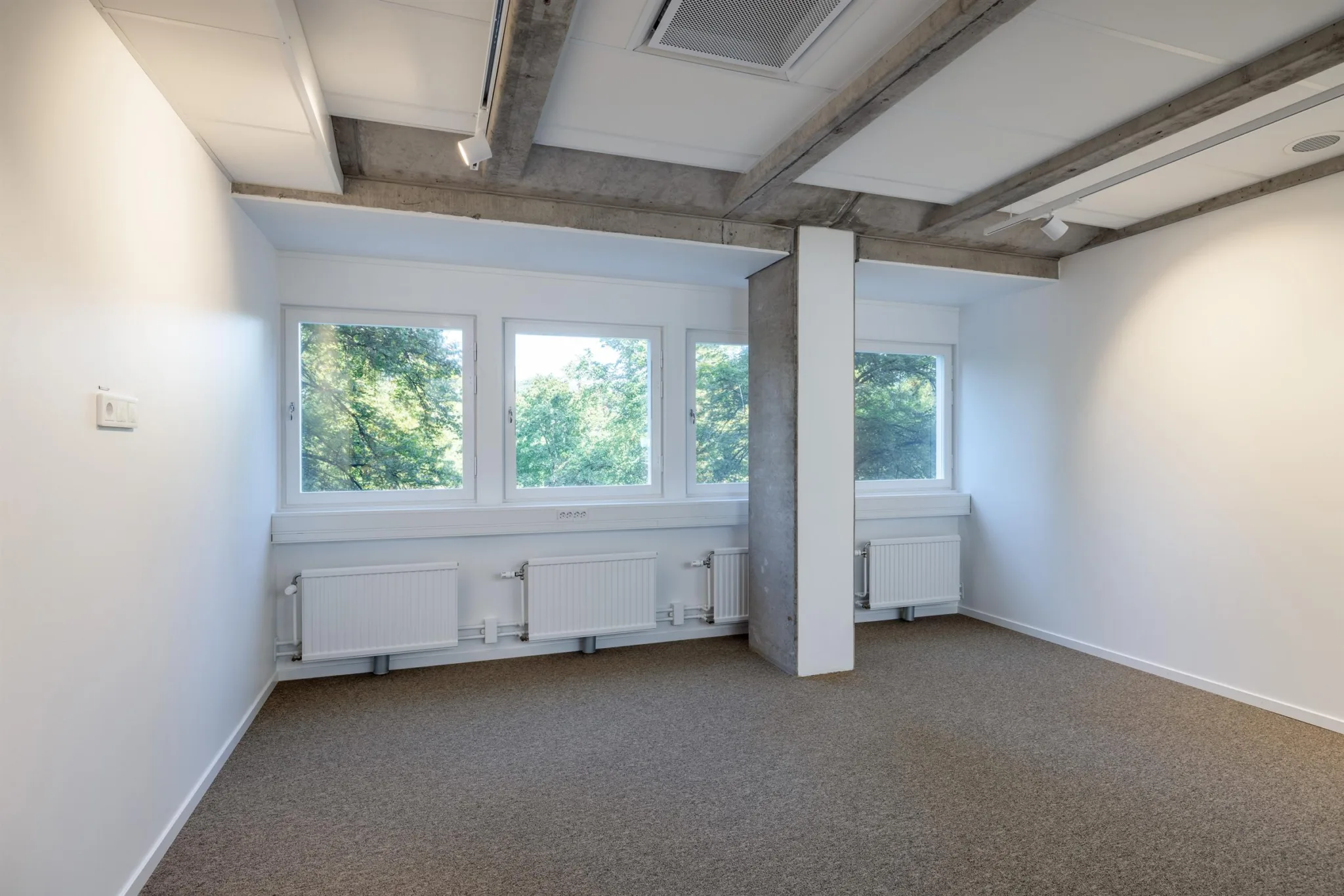 4. Ett mindre kontorsrum med tre fönster, vita väggar och beige matta.