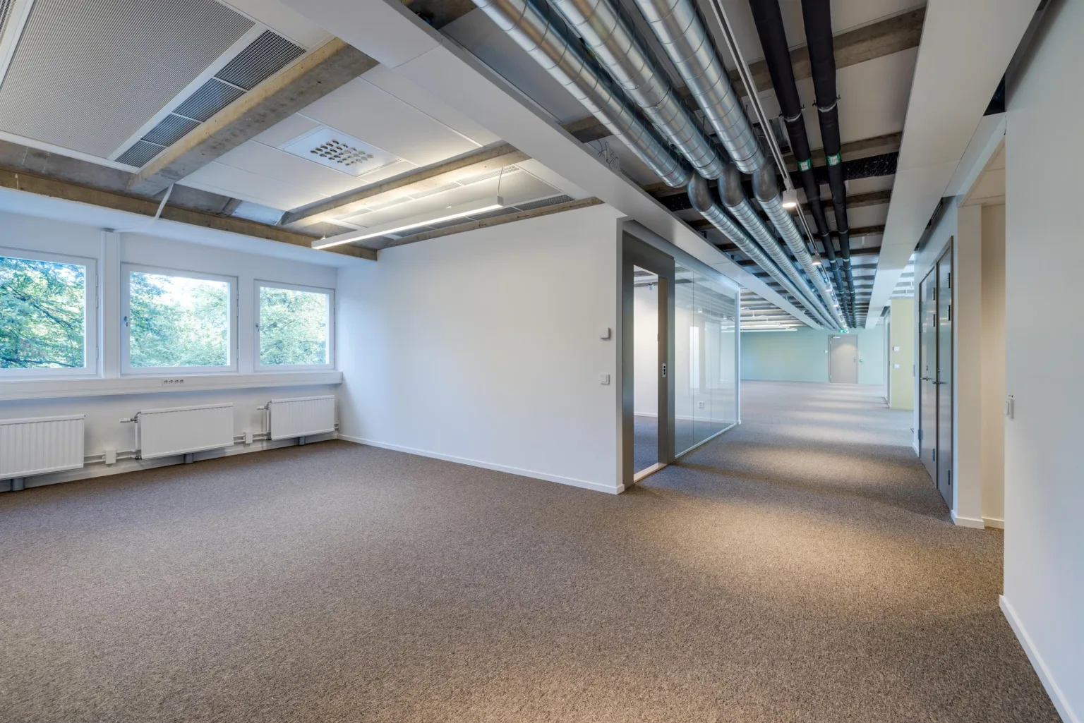 5. Ett öppet kontorsutrymme med beige matta, vita väggar och synliga rör i taket.