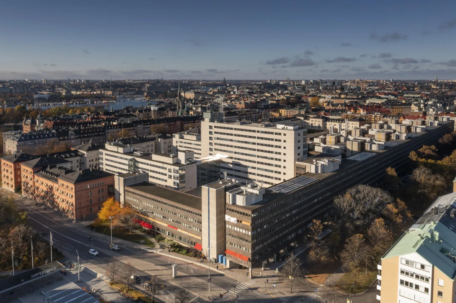 En flygvy över ett stort byggnadskomplex i stadsmiljö med omgivande gator och parker.