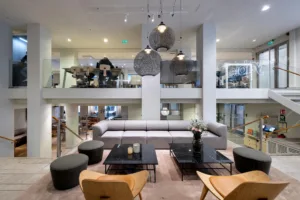 En modern loungemiljö med grå soffa, svarta bord och stora lampor hängande från taket.