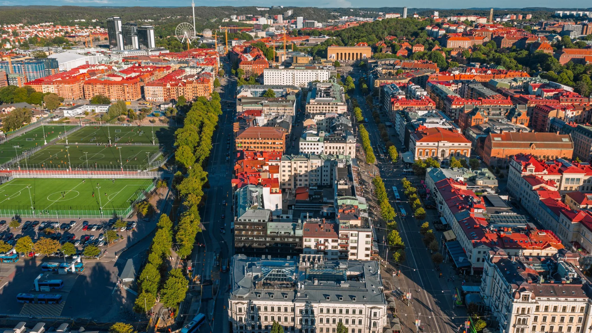 Flygbild av en stad med trädplanterad gata omgiven av röda tak och byggnader.