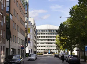 4. En stadsgata kantad av byggnader med ett stort vitt kontorshus i bakgrunden.