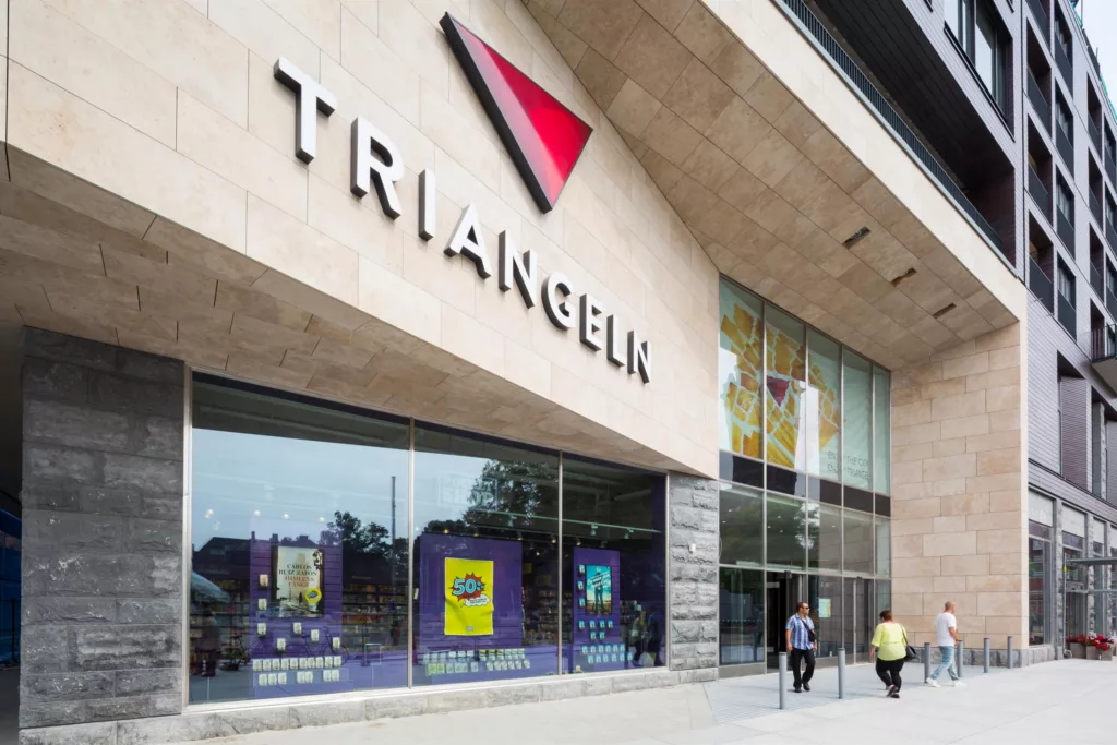 2. Entré till köpcentret Triangeln med en stor skylt, glasfönster och två personer som går förbi.