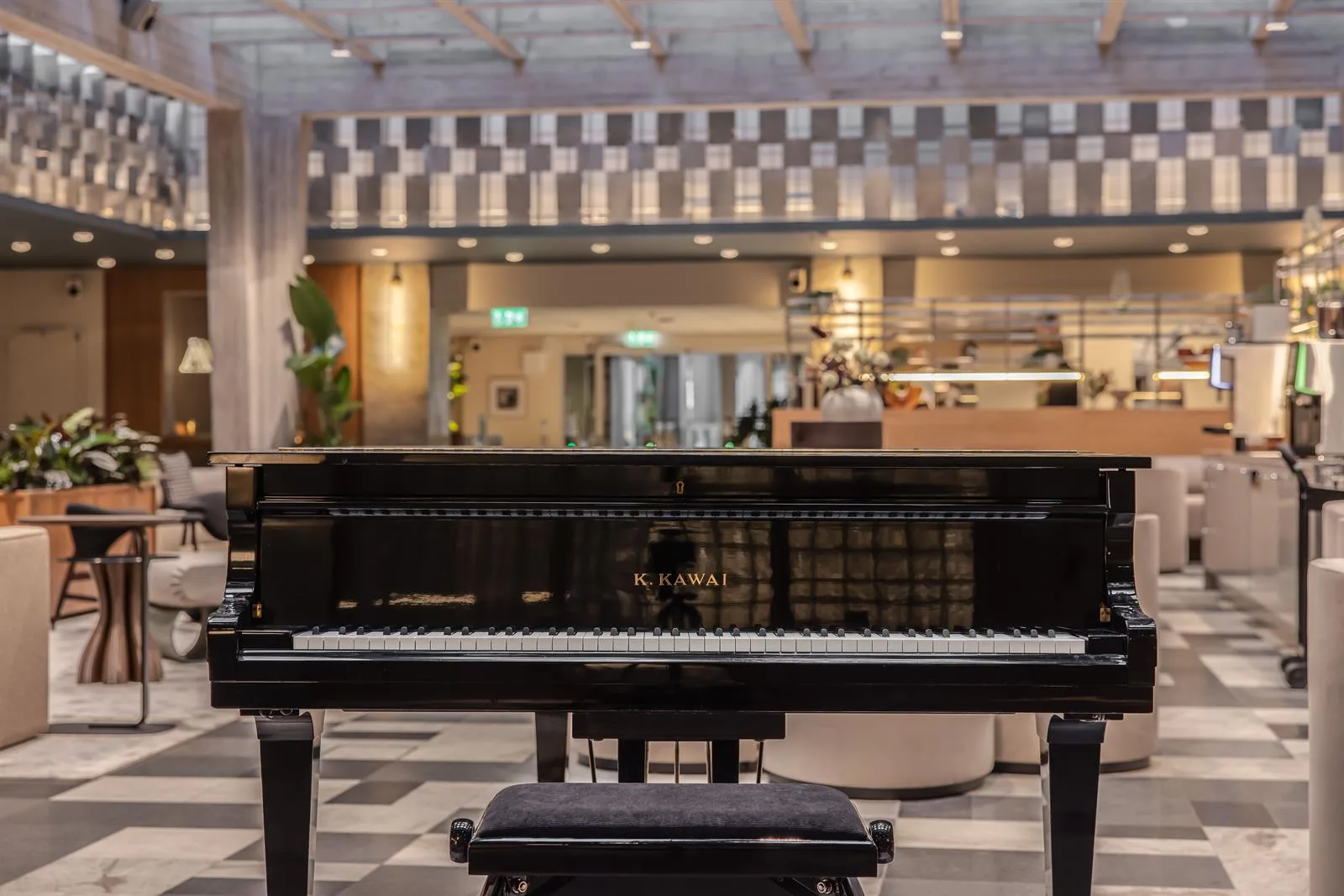 En svart flygel står i ett öppet utrymme med dekorativ belysning och en reception i bakgrunden.