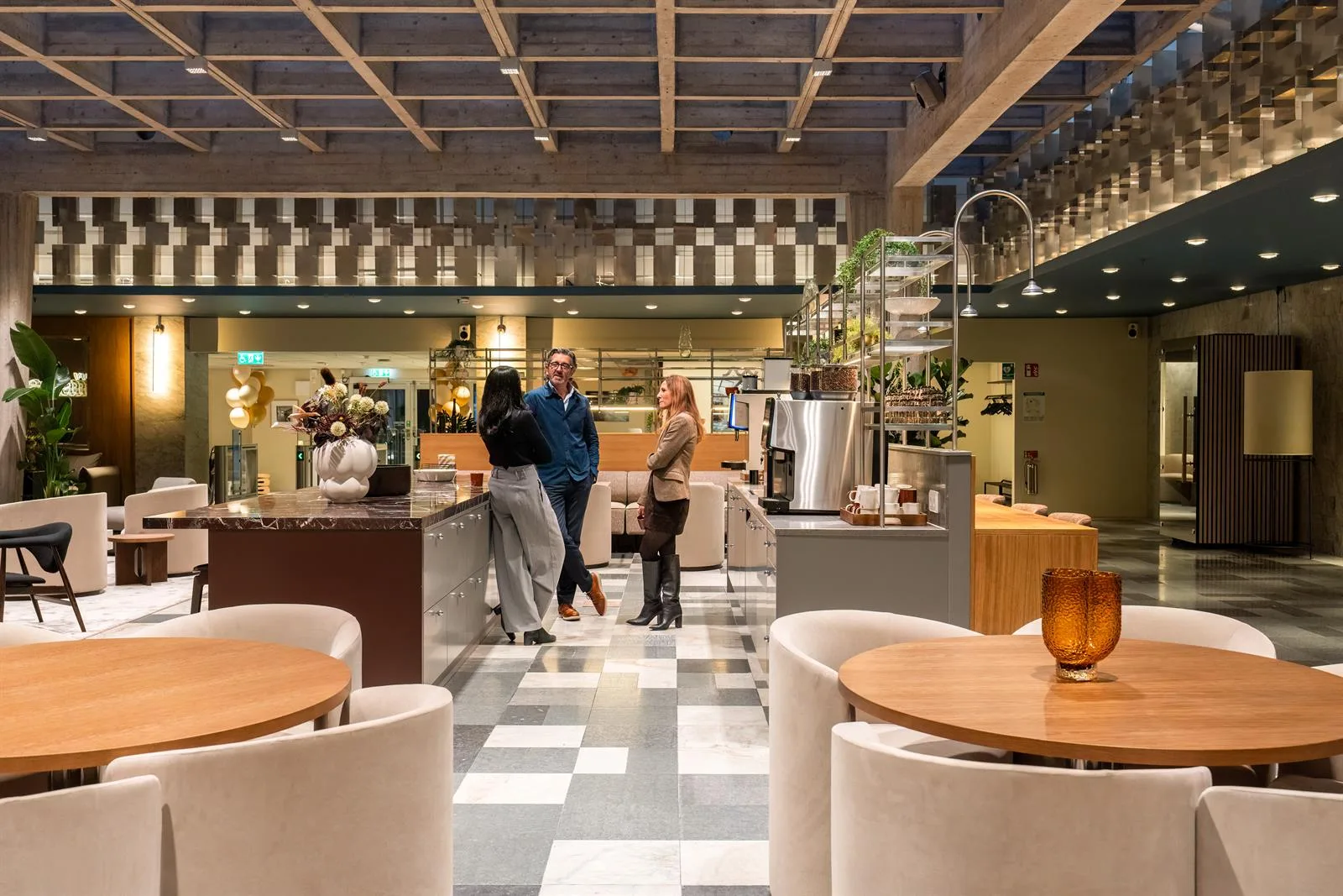 En modern kafémiljö med sittplatser, bord och personer som står vid disken och samtalar.