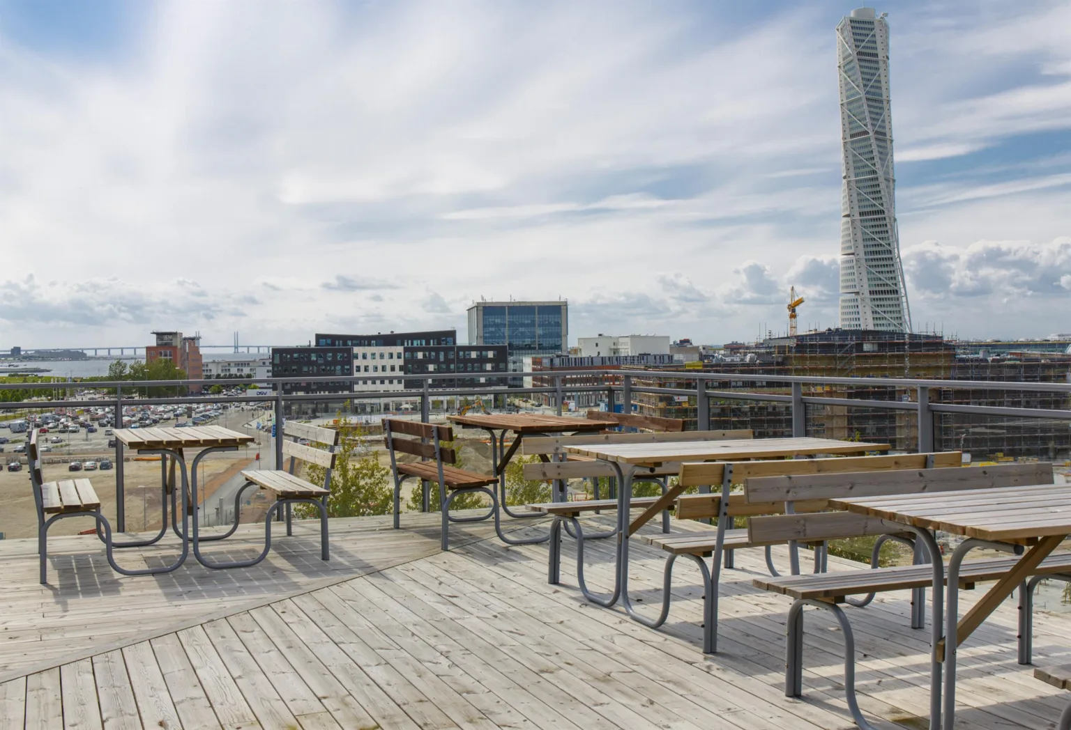 1. Flera träbord och bänkar står på en takterrass med utsikt över staden och Turning Torso i bakgrunden.