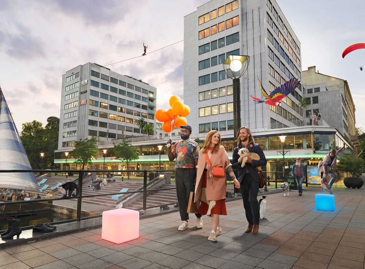 3. Tre personer promenerar på ett torg vid skymning, omgivna av moderna byggnader och dekorationer som färgglada ballonger.