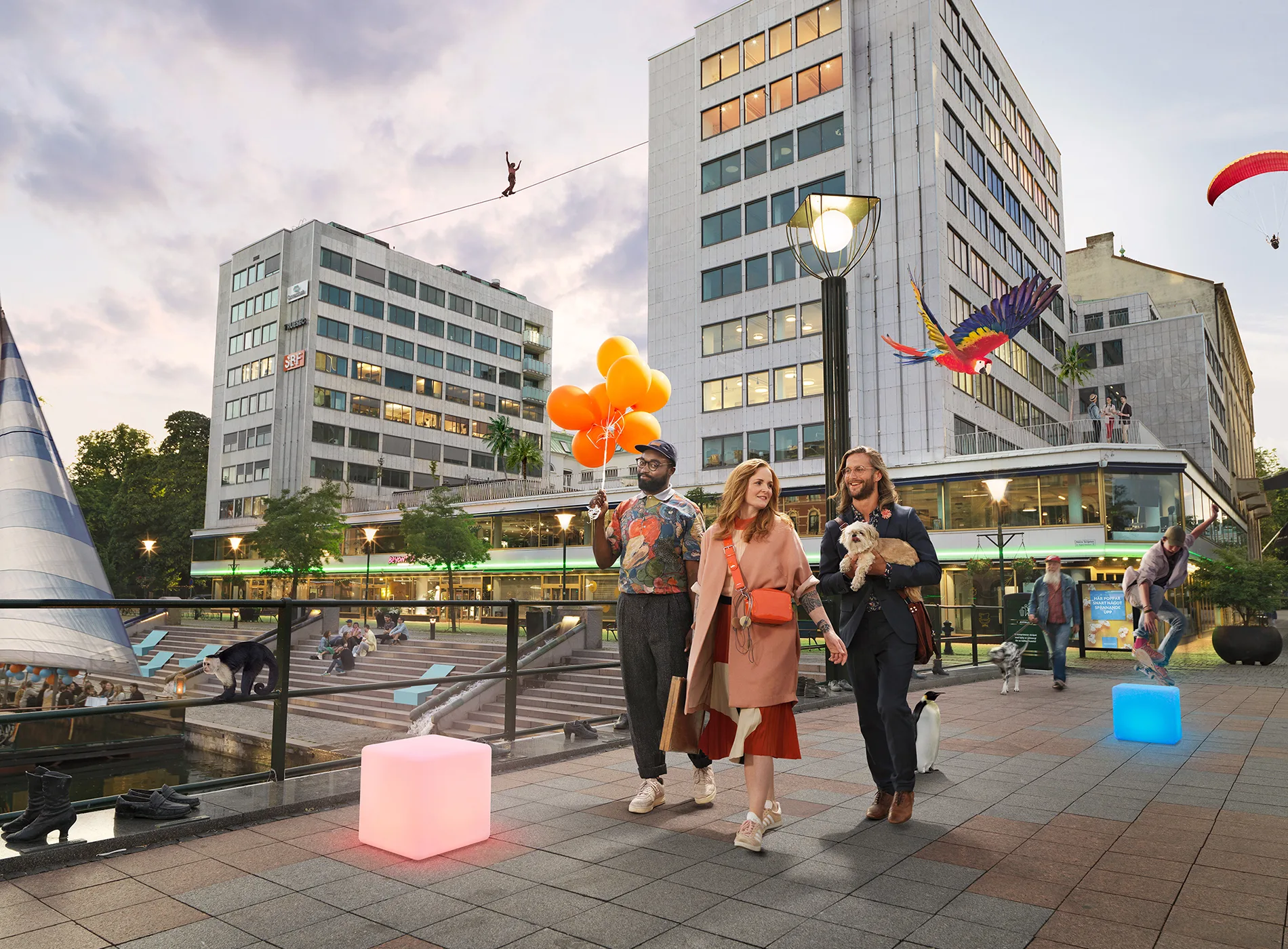 3. Tre personer promenerar på ett torg vid skymning, omgivna av moderna byggnader och dekorationer som färgglada ballonger.