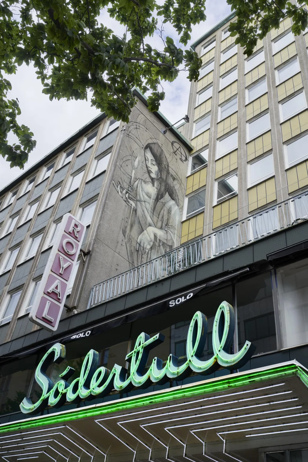 1. En byggnad med en stor väggmålning av en kvinna, en skylt med texten "HOTEL" och en neonskylt med texten "Södertull".