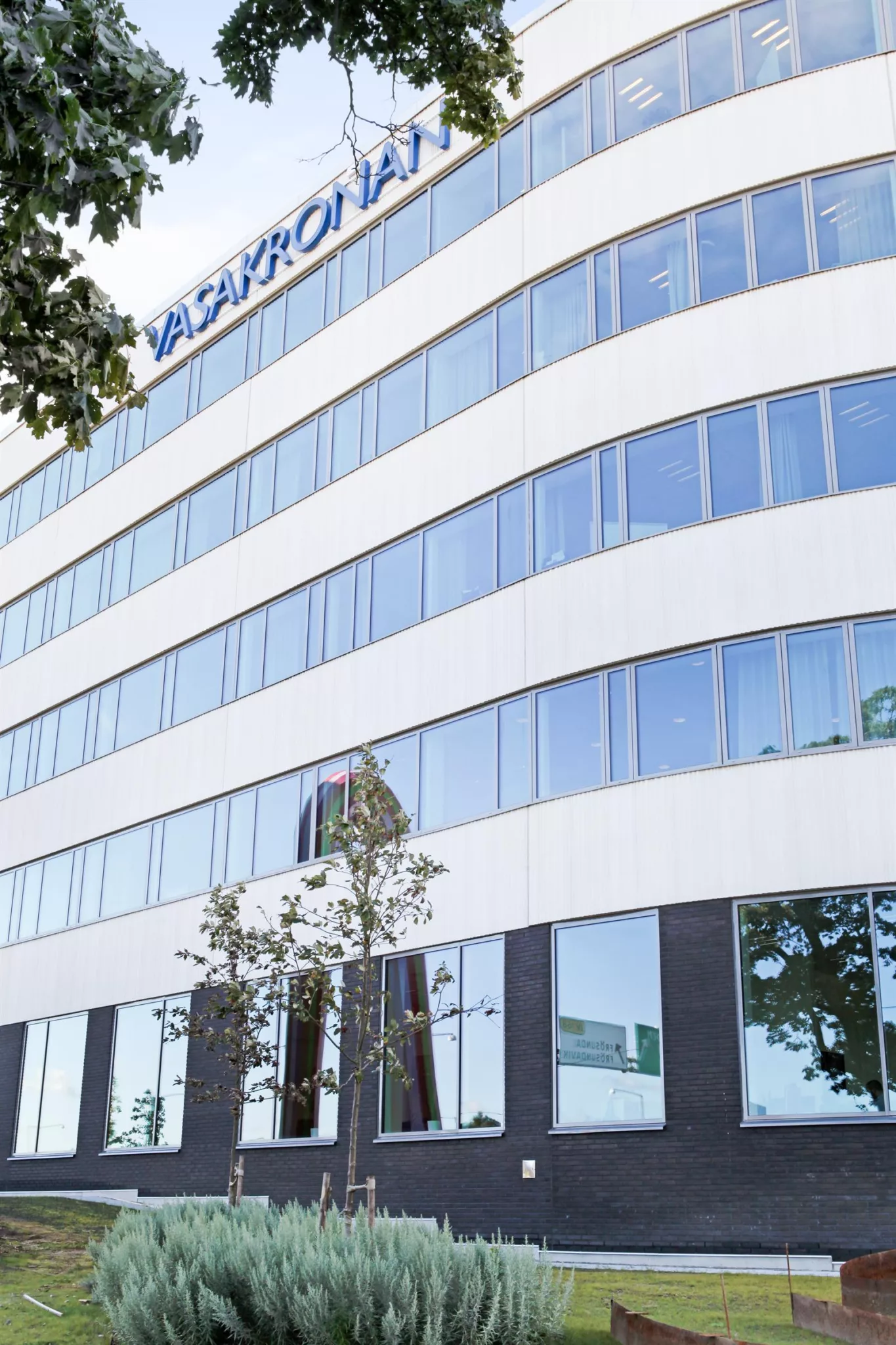 En vit kontorsbyggnad med välvda glasfönster och ett företagsnamn på toppen.