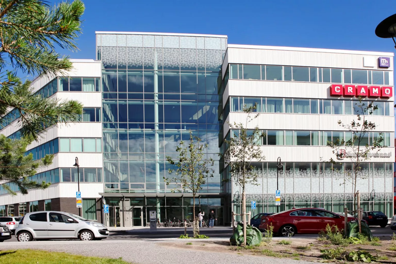 En kontorsbyggnad med stora glasfönster och parkerade bilar framför.