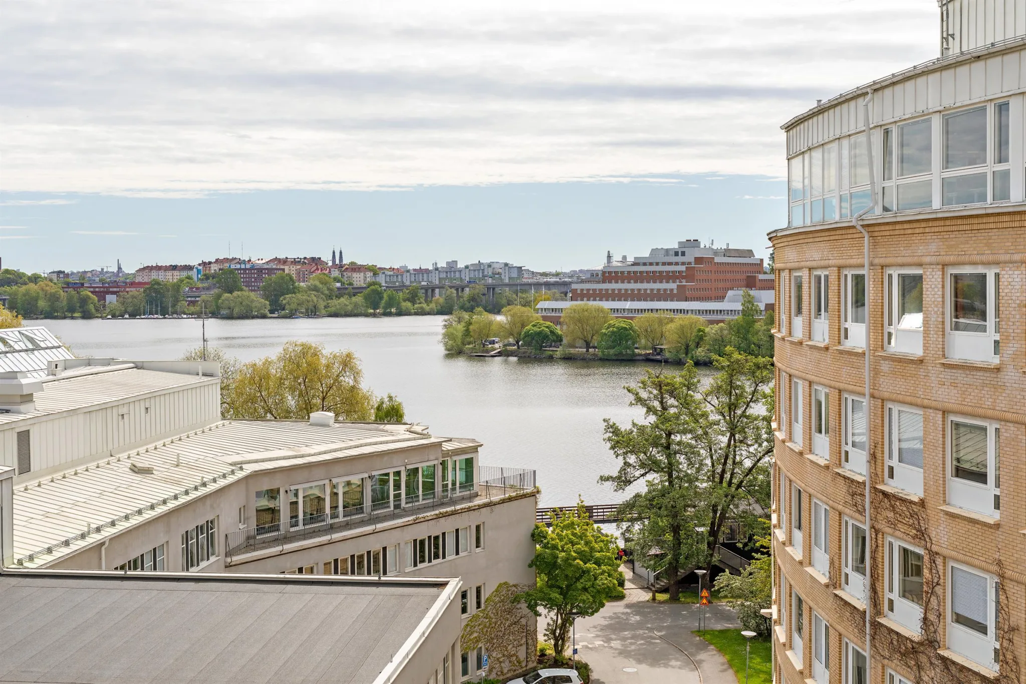 5. Utsikt över en lugn vattendrag omgiven av byggnader, träd och grönska under en molnig himmel.